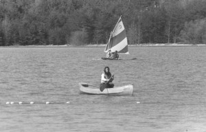 Two people on a sail boat and another person in a canoe on the lake