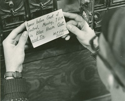 Man holding a summoning to the Court of Control Money, 7 P.M. in Blue Room. and to wear a coat and tie