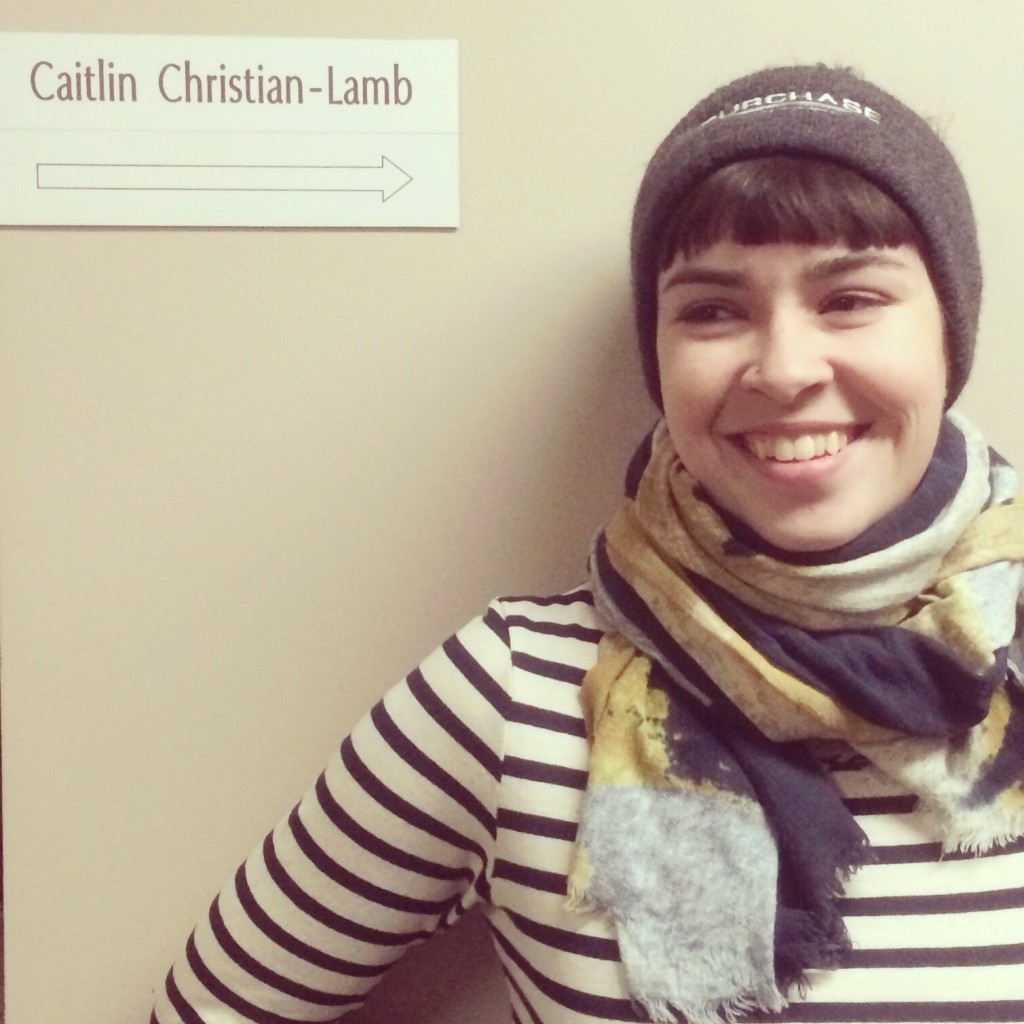 Caitlin Christian-Lamb next to a sign that says her name with an arrow pointing to her