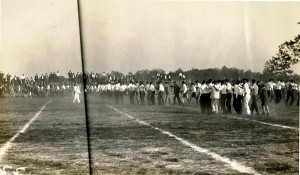 Many people standing in lines on the football field wearing black pants and white shirts