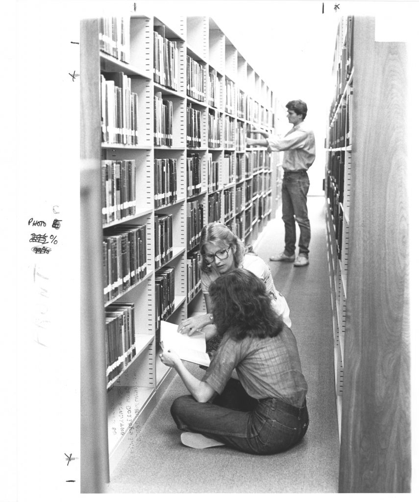 Three students work in an aisle of Little Library, circa early 1980s.