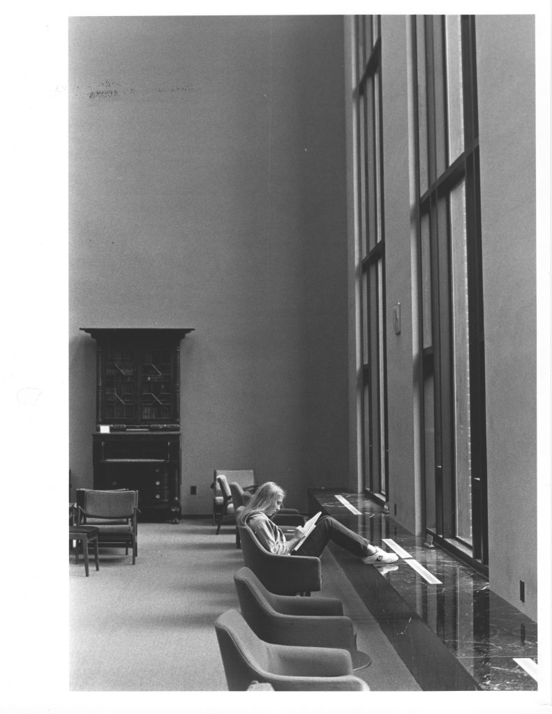 A student reads in front of the large windows in Little Library, circa early 1970s.