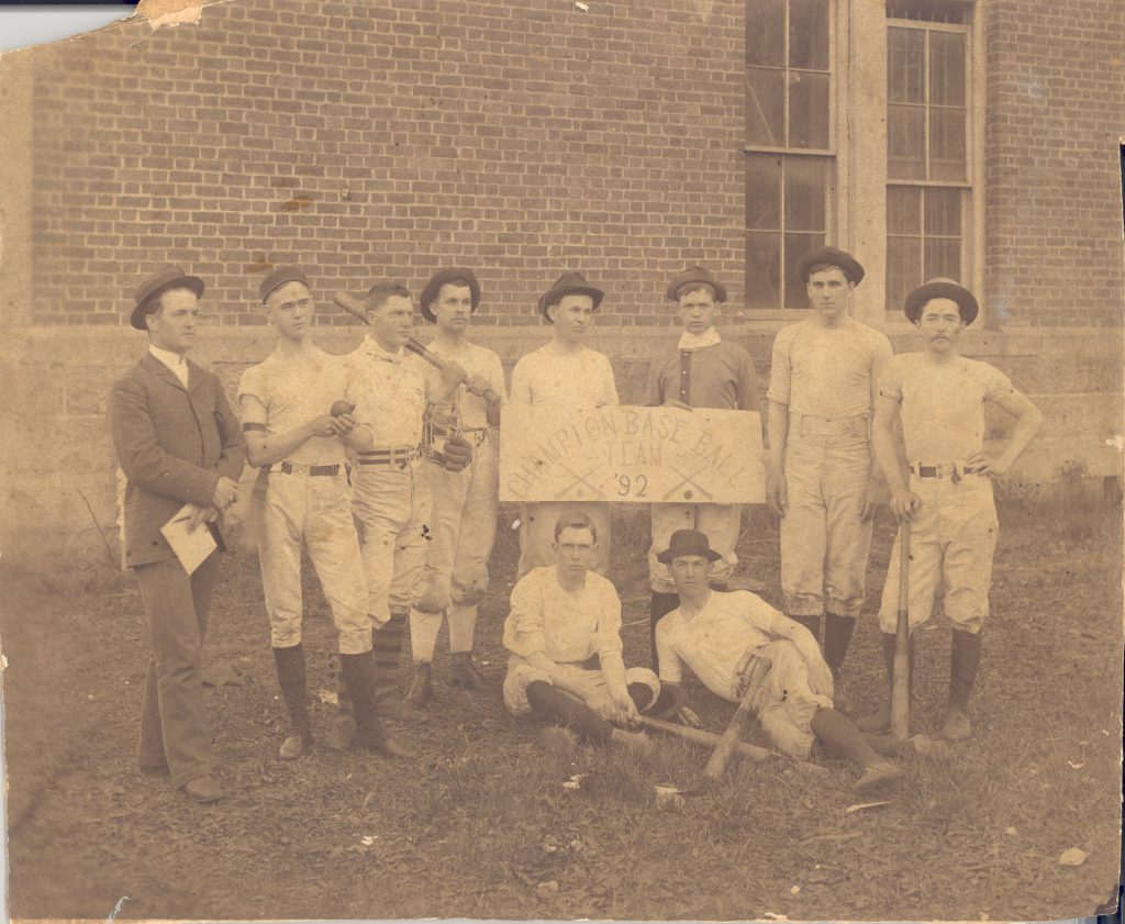 Members of the Class of 1892 baseball team, holding a sign indicating that their class had won the championship showdown between all class teams.