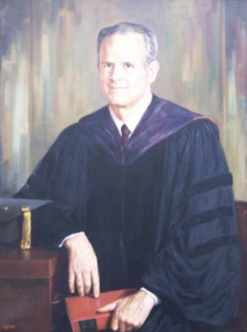 A portrait of a man in collegiate robes leans casually against his desk. His cap lies on the tabletop and he hold a bound leather book on his lap.