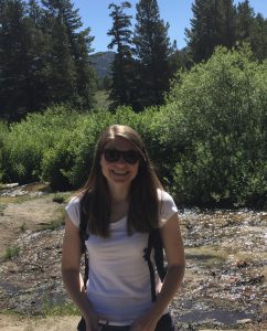 Woman on a mountain trail wearing a white t-shirt and black sunglasses.